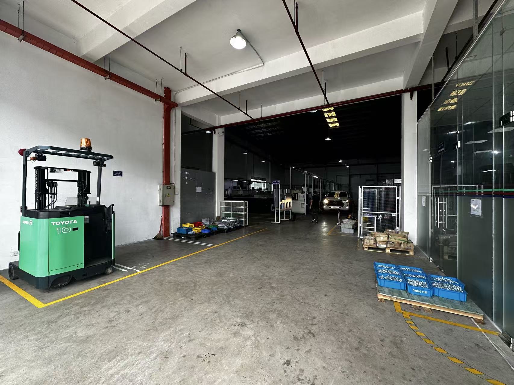 Factory loading area with a Toyota reach truck and finished parts bins near the glass office